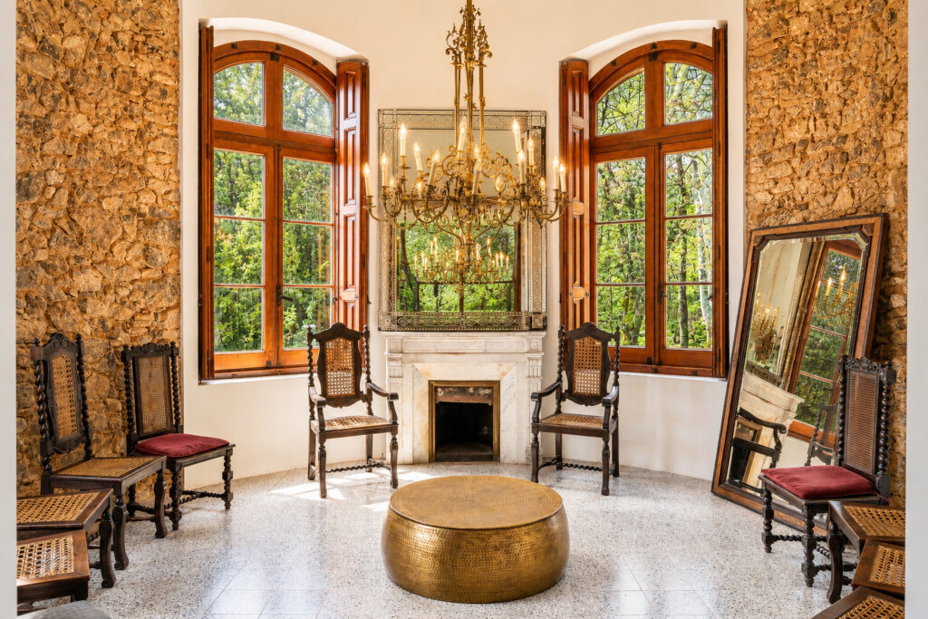 Sala circular de la torre con muros de piedra, ventanas arqueadas y vistas al jardín en un castillo de Girona